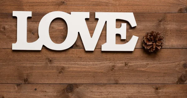 Biały tekst miłości i sosna stożek dekoracji na drewnianym tle — Zdjęcie stockowe