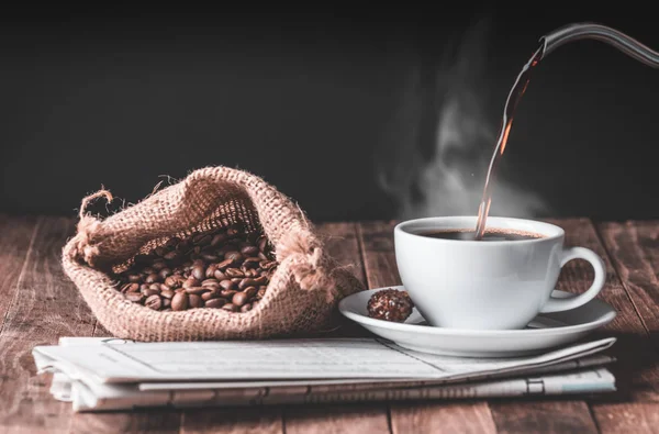 Šálek kávy, skořicová tyčinka, pražená kávová zrna a noviny na — Stock fotografie