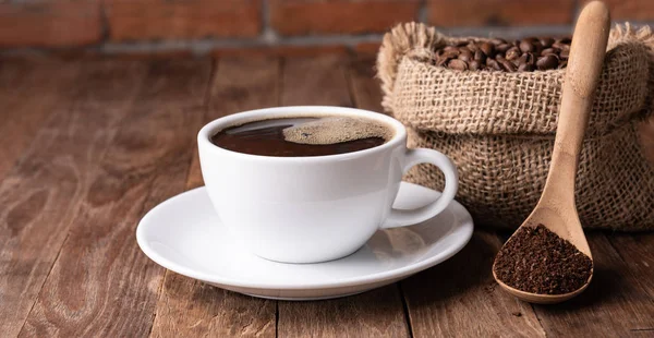 Taza de café, café molido y granos de café en arpillera sobre tabla de madera —  Fotos de Stock