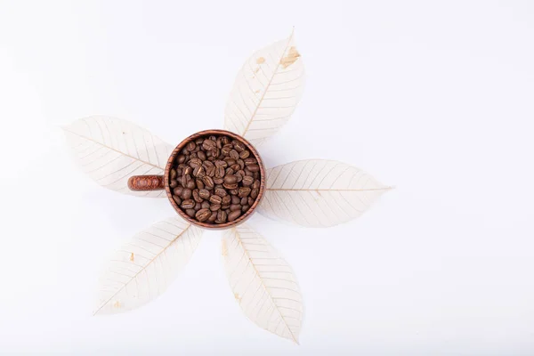 Grãos de café torrados em xícara de madeira sobre fundo de folha seca — Fotografia de Stock