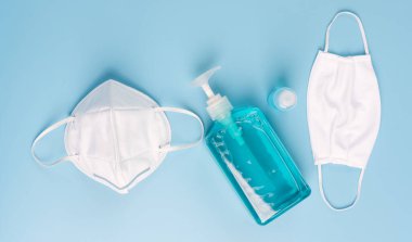 Beyaz maske mikrop koruması ve jel alkolü ya da el dezenfektanı şişesi. Mavi arka plandaki Corona virüsünden korunmak için el yıkama spreyi.