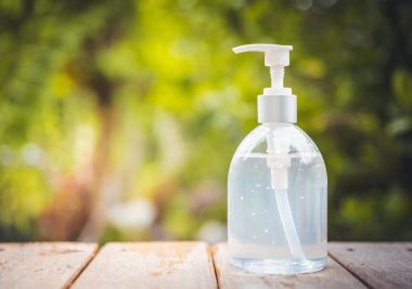 Beyaz el dezenfektanı ya da alkol pompası şişesi ahşap üstünde yeşil arka planda.