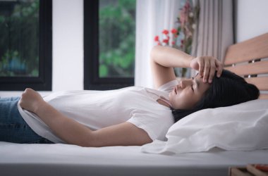 Beyaz tişörtlü güzel bir kadın ve mavi kot pantolon daha iyi, sağlıklı ve ilaç konsepti için yatakta baş ağrısı ve soğuk alır.