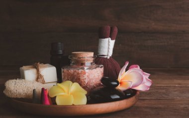 Organik sabun, luffa ovma, sıkıştırma topu, pembe tuz, siyah taşlar ve ahşap arka planda ahşap tepside güzel plumerai çiçekli spa ürünleri. 