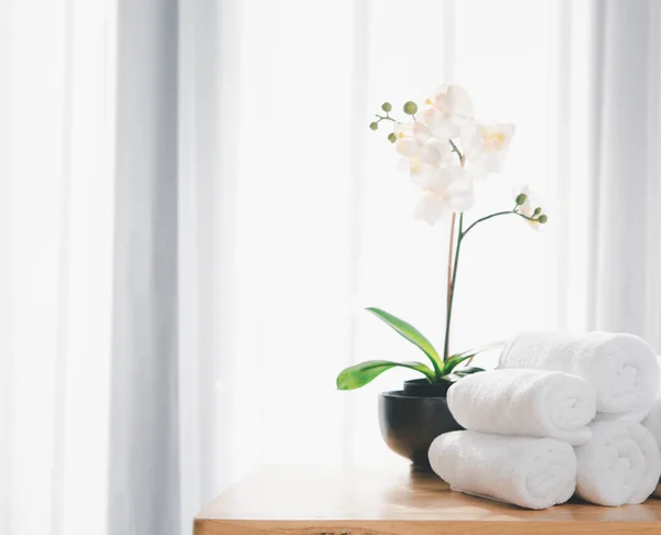 木制桌子上有洁白的毛巾和美丽的兰花 背景上有模糊的白色浴室 — 图库照片