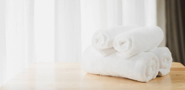 White  soft towels folded on wood table with blurred white bathroom background