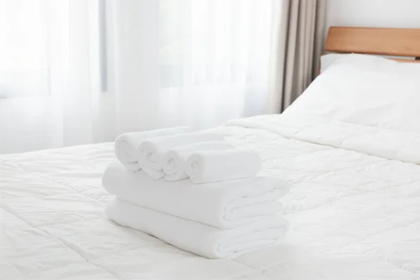 Stack of white towels on white bed in modern bedroom