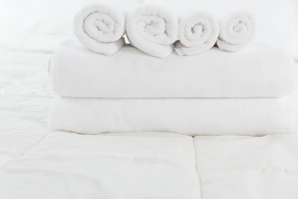 Stack of white towels on white bed in modern bedroom