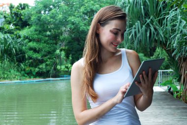 Parkta akıllı telefon oynayan genç kadın.