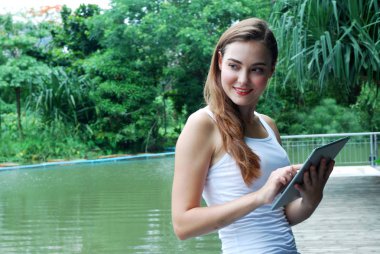 Parkta akıllı telefon oynayan genç kadın.