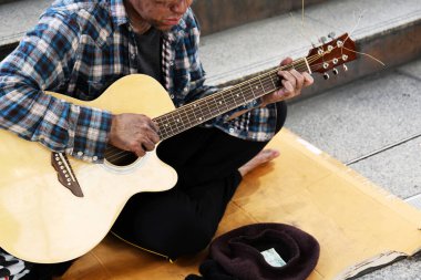 Yürüyen sokakta akustik gitar çalan evsiz adam.