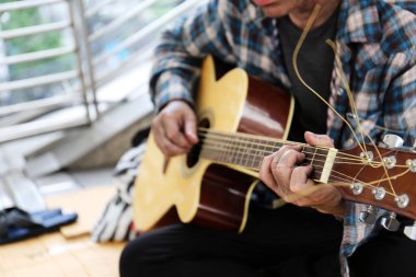 Yürüyen sokakta akustik gitar çalan evsiz adamın yakın çekim eli.