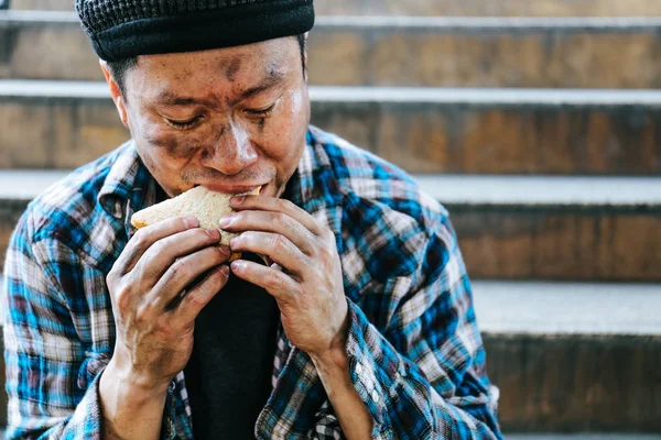 Close-up homeless man portrait eating bread on walking street.