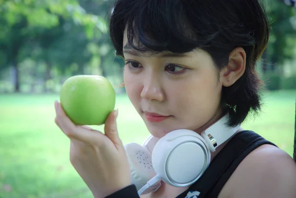 緑のリンゴを持ち 公共の公園を歩く美しいアジアのスポーツ女性 — ストック写真
