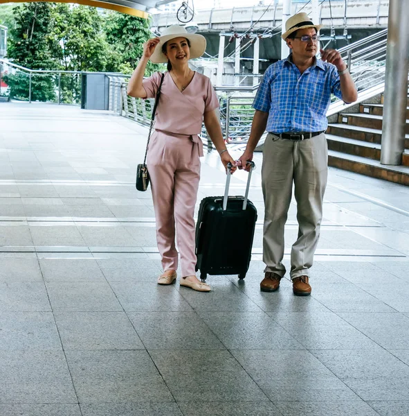 senior couple drag luggage traveling on walking street