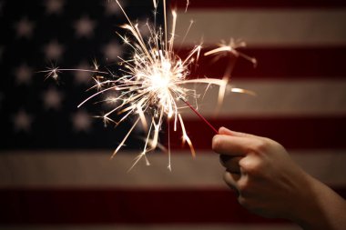 4. Için Amerikan Bayrağı önünde yanan kıvılcım tutan el 