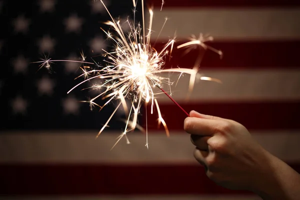Mão segurando sparkler aceso na frente da bandeira americana para 4th — Fotografia de Stock