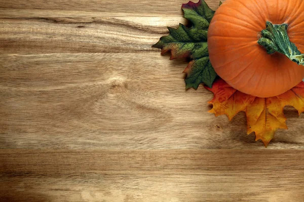 Pompoen en herfstbladeren op houten ondergrond — Stockfoto