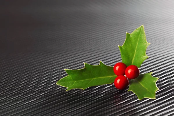 Acebo de Navidad verde brillante con bayas rojas en fibra de carbono oscuro —  Fotos de Stock