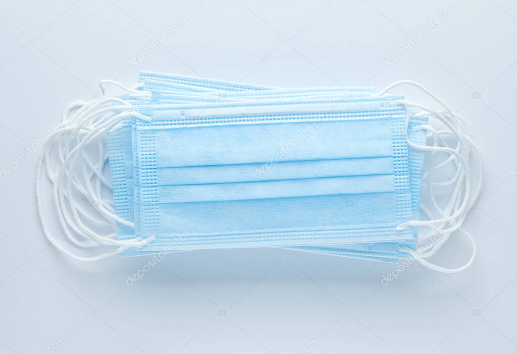Pile of disposable medical face masks on blue background. Personal protective equipment, PPE.