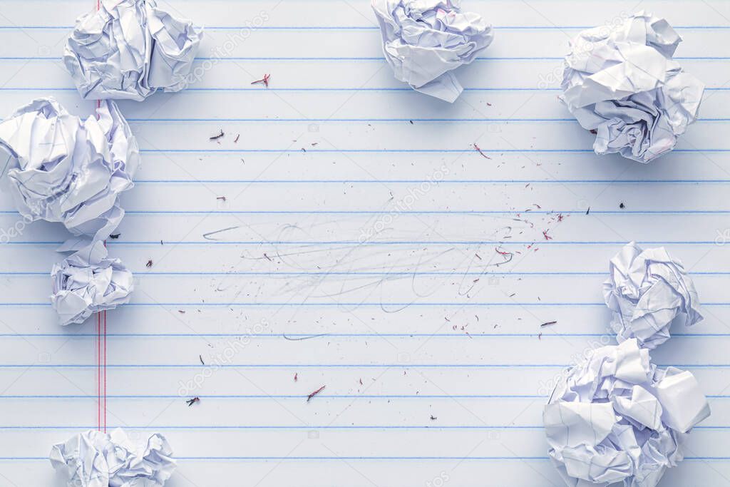 School supplies of blank lined notebook paper with eraser marks and erased pencil writing, surrounded by more trashed balled up paper. Studying or writing mistakes concept.