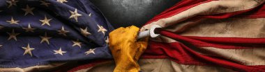 İngiliz anahtarı tutan ve yıpranmış Amerikan bayrağı tutan iş eldiveni. Amerikan yapımı, Amerikan işgücü, mavi yakalı işçi, veya İşçi Bayramı konsepti.
