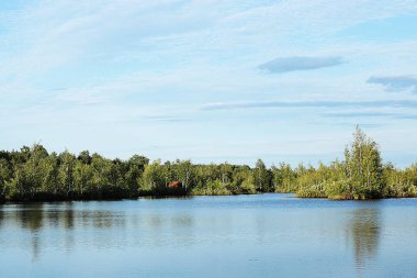 Doğal göl, bulutlar ve birçok ağaç ve sakin berrak su ile yeşil orman ile mavi gökyüzü