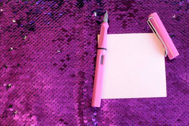 Payetler parlar ve parıltılar ile parlak pembe arka plan kumaş üzerinde bir kapak yalan ile notlar dolma kalem için kağıt bir parça, kayıtlar için boş alan
