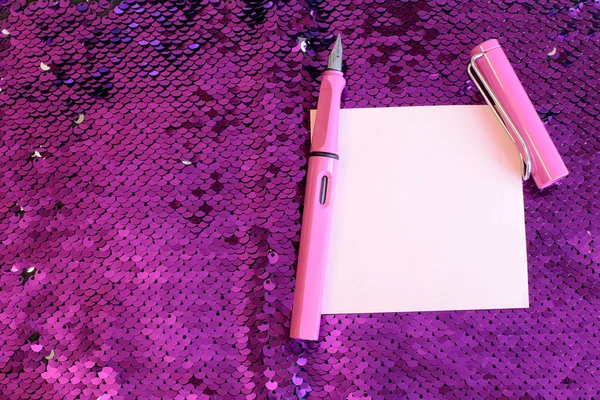 一张纸笔记喷泉笔与帽子躺在明亮的粉红色背景织物与亮片光泽和闪闪发光 自由空间的记录 — 图库照片