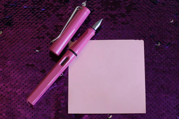 一张纸笔记喷泉笔与帽子躺在明亮的粉红色背景织物与亮片光泽和闪闪发光 自由空间的记录 — 图库照片