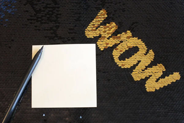 A sheet of paper for records and a  felt-tip pen lie on a bright black shiny background, the fabric with sequins shines and shimmers, free space for records