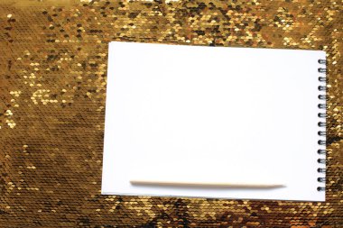 Boş beyaz çarşaflar ve ahşap kazıyıcı ile bir defter altın payetler parlak parlak bir arka plan üzerinde, notlar yazmak için bir yer, beyaz kağıt üzerine bir hatırlatma metni yazmak