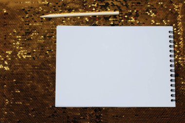 Boş beyaz çarşaflar ve ahşap kazıyıcı ile bir defter altın payetler parlak parlak bir arka plan üzerinde, notlar yazmak için bir yer, beyaz kağıt üzerine bir hatırlatma metni yazmak