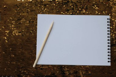 Boş beyaz çarşaflar ve ahşap kazıyıcı ile bir defter altın payetler parlak parlak bir arka plan üzerinde, notlar yazmak için bir yer, beyaz kağıt üzerine bir hatırlatma metni yazmak