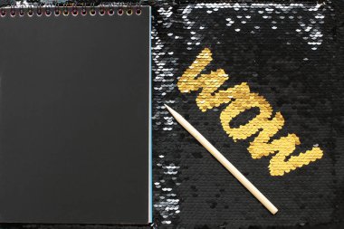 Siyah payetler ve siyah çarşaf ve girişleri için ahşap bir kazıyıcı alanı ile bir not defteri bir arka plan üzerinde altın payetler Wow harfleri