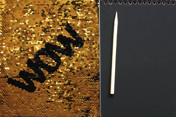 WOW letters from black sequins on a background of gold sequins and a notepad with black sheets and a wooden scraper, plenty of space for entries to record your words