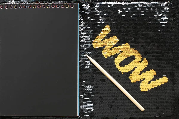 WOW letters of gold sequins on a background of black sequins and a notepad with black sheets and a wooden scraper space for entries