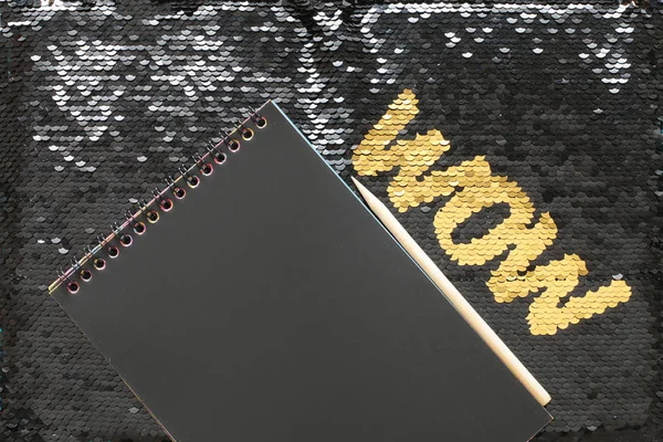 WOW letters of gold sequins on a background of black sequins and a notepad with black sheets and a wooden scraper space for entries