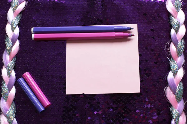 Pink sheet of note paper and pink and purple felt-tip pens on a dark pink background fabric with sequins shines and shimmers and a pigtail of shiny threads, free space for records