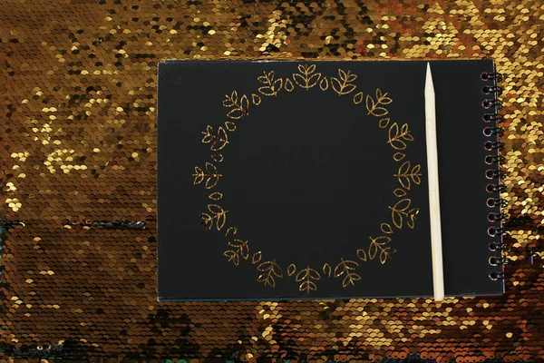 空の黒いシートと木製のスクレーパーを持つノートブックは 金のスパンコール ノートを記録するためのスペースの明るい光沢のある背景にあり 黒い紙にリマインダーテキストを書きます — ストック写真