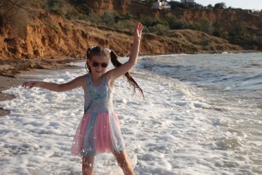 Uzun kahverengi saçlı sekiz yıllık biraz yaramaz ve neşeli kız dalgalar üzerinde atlar ve yaz tatili keyfi ile gülüyor