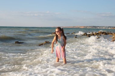 Uzun kahverengi saçlı sekiz yıllık biraz yaramaz ve neşeli kız dalgalar üzerinde atlar ve yaz tatili keyfi ile gülüyor