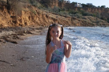 Uzun kahverengi saçlı sekiz yıllık biraz yaramaz ve neşeli kız dalgalar üzerinde atlar ve yaz tatili keyfi ile gülüyor