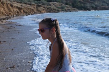 Uzun kahverengi saçlı sekiz yıllık biraz yaramaz ve neşeli kız dalgalar üzerinde atlar ve yaz tatili keyfi ile gülüyor