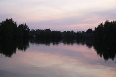 Parktaki gölde gün batımı şafağın güzelliğinin mucizesi sudaki ağaçların yansıması.