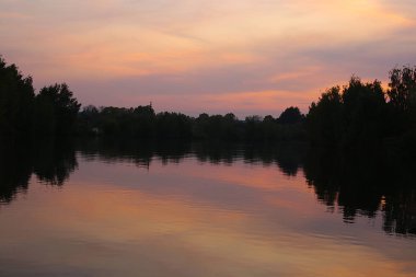 Parktaki gölde gün batımı şafağın güzelliğinin mucizesi sudaki ağaçların yansıması.