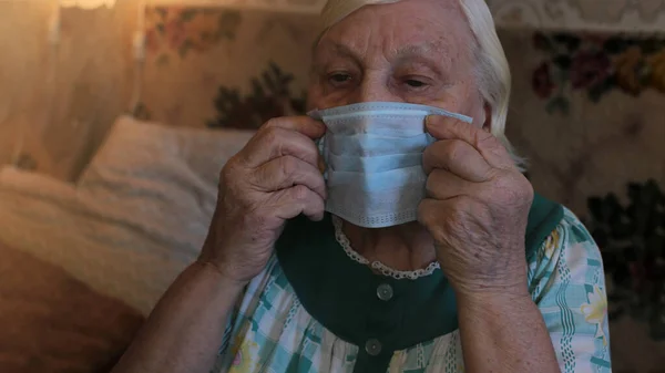 Blue medical mask in the hands of an old gray-haired grandmother, put on and wear a respirator to guard against viruses