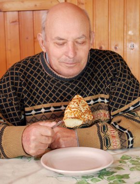 Dacha'daki büyükbaba krep yemek için oturdu. Mutfakta iyi bir ruh hali içinde yaşlı kişi bir masada oturur ve kahvaltı çatal ile krep yiyor.
