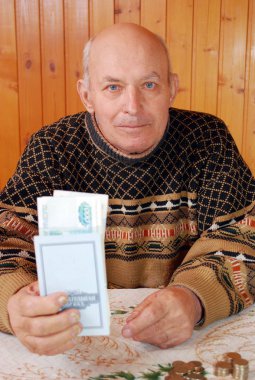 Dacha dede bir masada oturur ve elinde kapalı tasarruf defteri ve kağıt notlar tutar. Yaşlı kişi tasarruf defterinde emeklilik ödeme ile bir masada oturur.