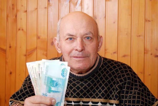 Dacha dede bir masada oturur ve elinde kağıt notlar tutar. Yaşlı kişi bir masada oturur ve elinde para tutar.